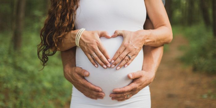 Expectant parents form a heart on mom's pregnant baby bump.